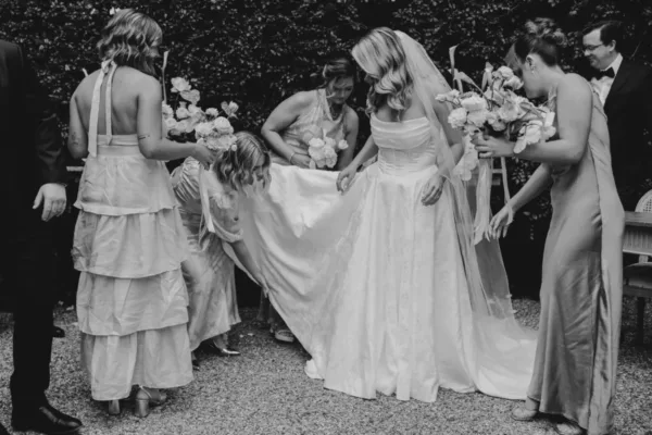 Bridesmaids and groomsmen carrying the bride’s dress train in a candid black-and-white wedding photograph.