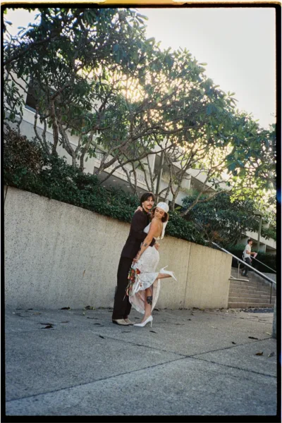 Bride and groom posing outdoors beside a concrete wall, captured on 35mm film.