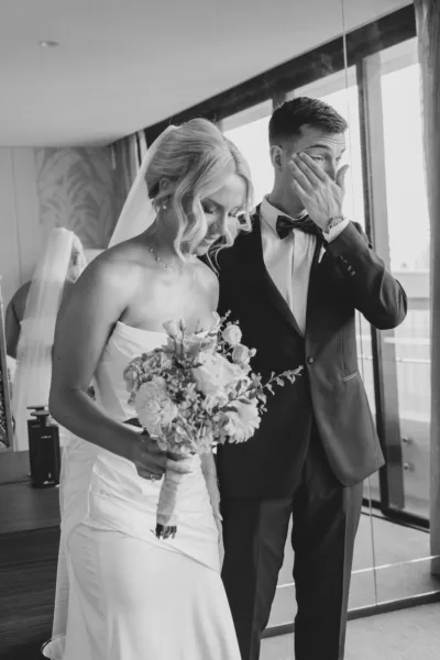 Bride holding her bouquet beside an emotional groom wiping away tears before the wedding ceremony.