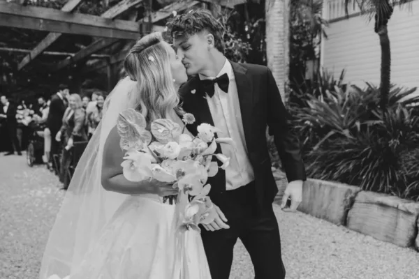 Bride and groom kissing after their black-tie wedding ceremony in a candid black-and-white portrait.