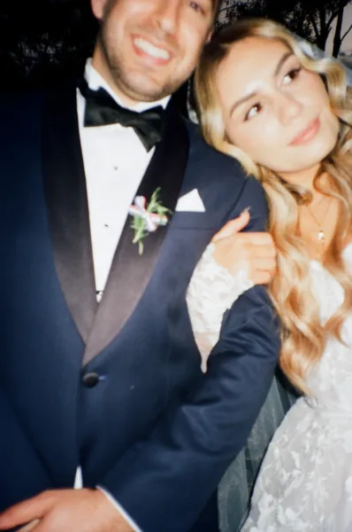 Close-up portrait of a bride and groom in black-tie wedding attire, photographed in a relaxed editorial style.