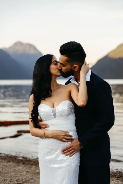 Bride and groom kissing at Alouette Lake with the sun setting on the mountains and lake behind them
