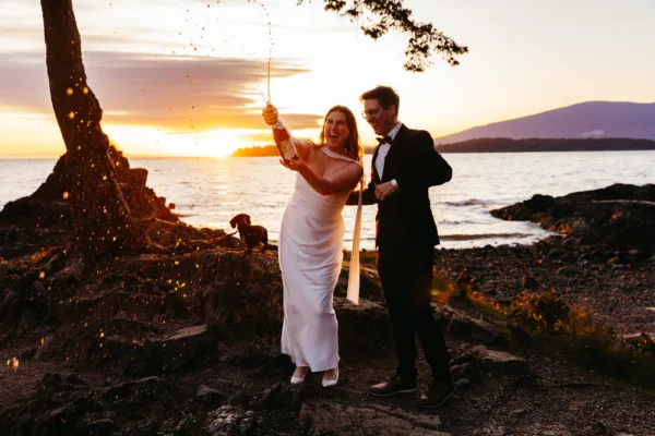 Bride and groom popping champagne to celebrate their elopement on Bowen Island, with their weiner dog