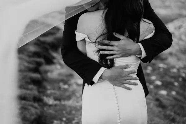 black and white portrait of the back of the bride and the grooms hands holding her