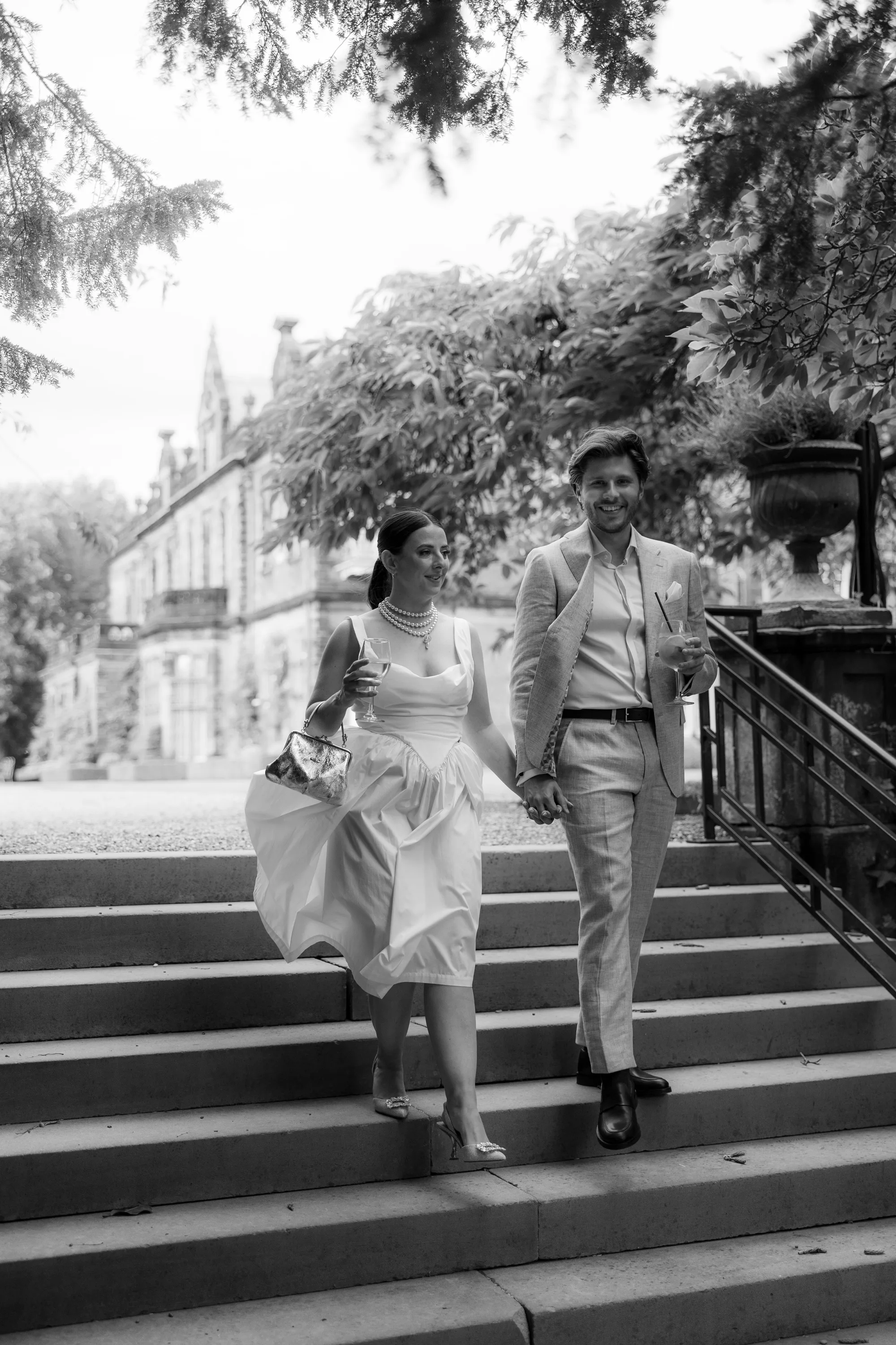 Capesthorne Hall Summer Wedding Jessica Sharpe Wedding Planner Jono Symonds Love My Dress.184 - Sophie & Dimitri's Beautiful, Relaxed & Elegant Wedding Weekend at Capesthorne Hall in Cheshire Bride wearing a Vivienne Westwood dress wiht large choker style pearls walking down a stone staircase in the gardens at Capesthorne Hall in Cheshire, with her groom to be in a pale suit.