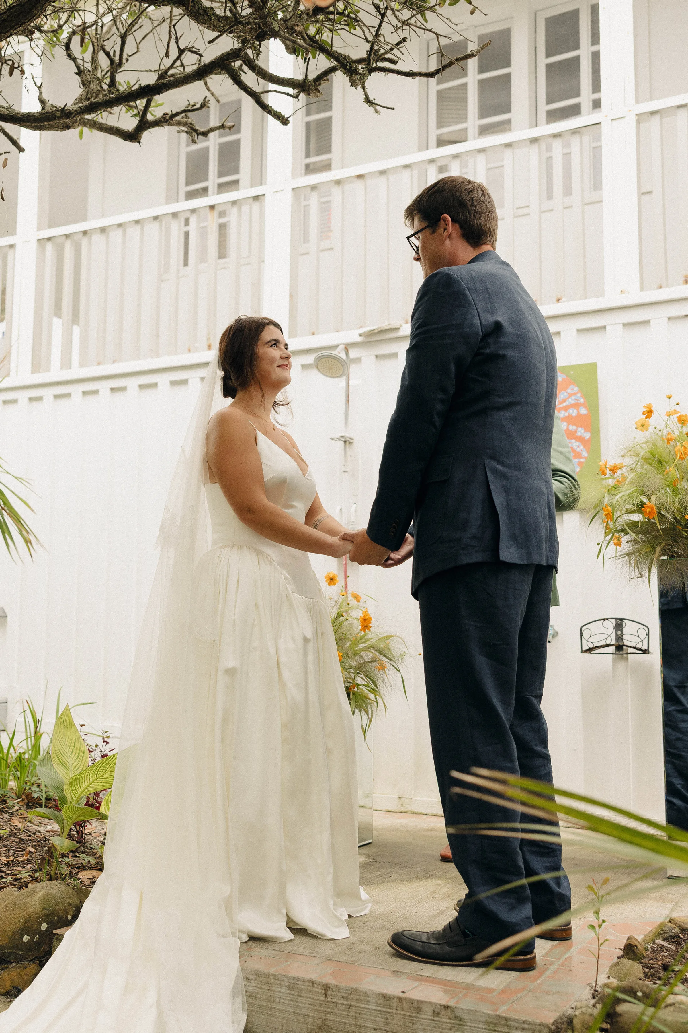 Danielle Frankel Bride Leslie DeAnne Photography.45 - Olivia in Danielle Frankel for her Intimate, Modern & Non-Traditional Wedding Bride and groom gazing into each other's eyes lovingly as they hold hands during their wedding ceremony vow exchange. She wears a Danielle Frankel gown and they are surrounded by orange and green flowers.