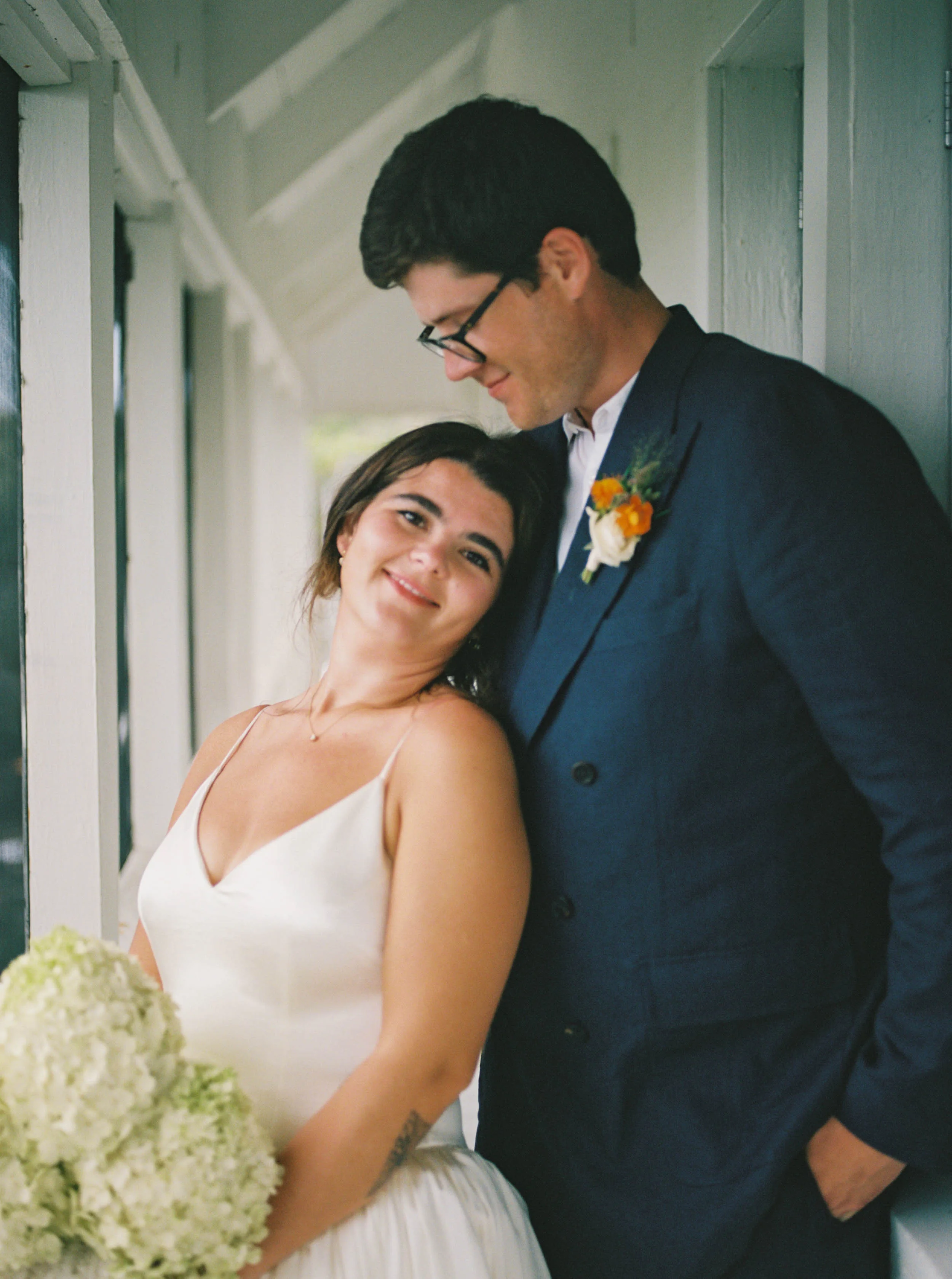 Danielle Frankel Bride Leslie DeAnne Photography.58 - Olivia in Danielle Frankel for her Intimate, Modern & Non-Traditional Wedding Sweet portrait of bride and groom after their wedding ceremony. She is leaving back into her groom who wears a blue shirt with an orange bouttonierre. The bride wears Daniel Frankel and carries a bouquet of hydrangea.