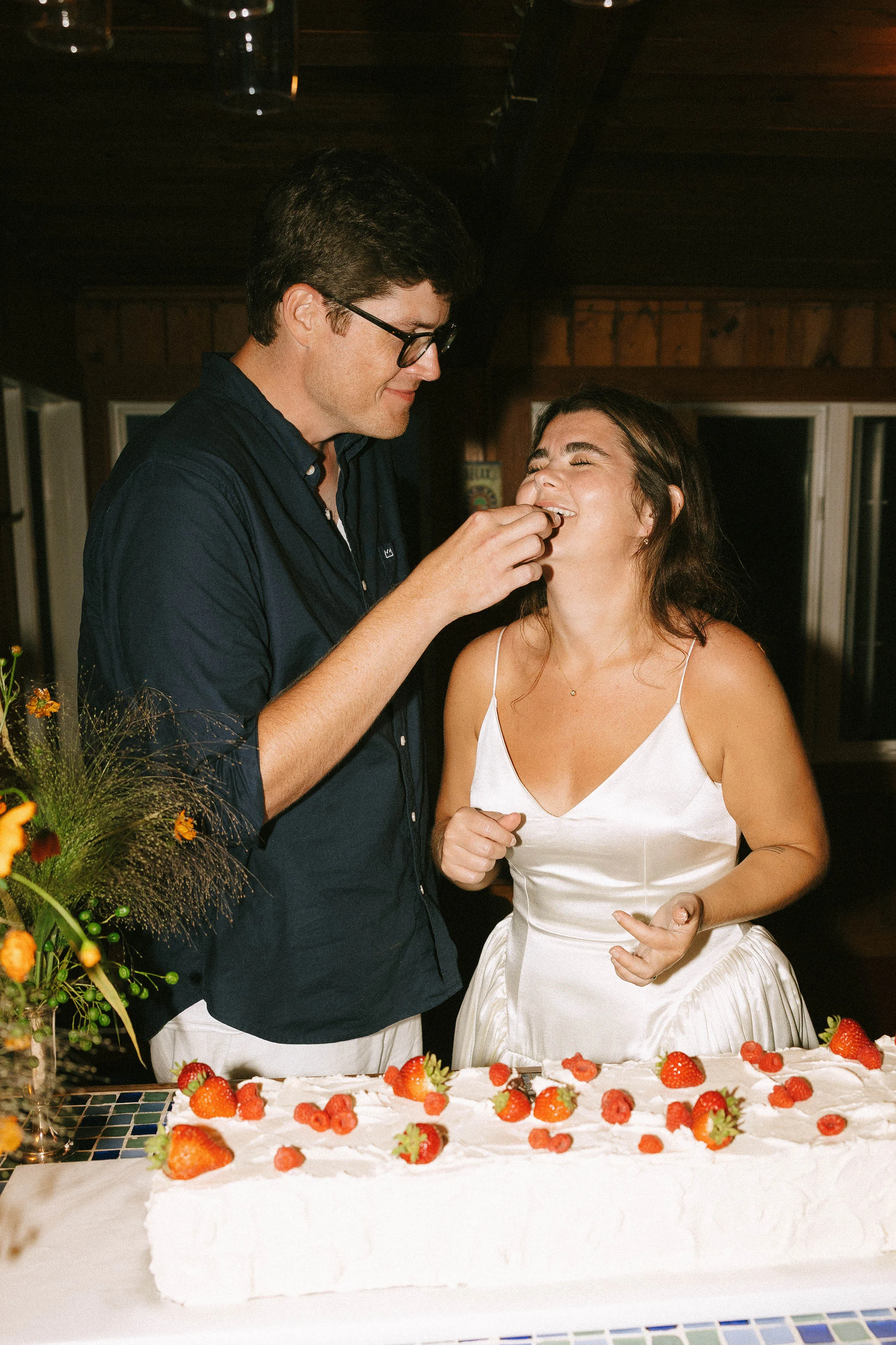 Danielle Frankel Bride Leslie DeAnne Photography.95 - Olivia in Danielle Frankel for her Intimate, Modern & Non-Traditional Wedding Bride and groom feeding one another slices of a long wedding cake with berries on top.