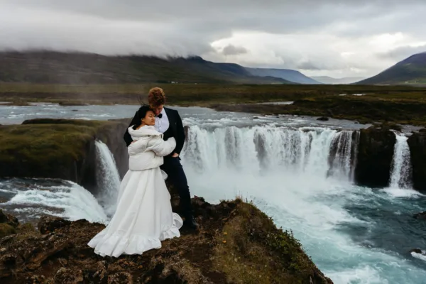 Bride and groom embracing in the cold with Godafoss behind them