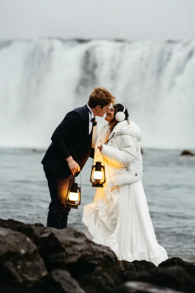Bride and groom kissing with lanterns with Godsfoss behind them