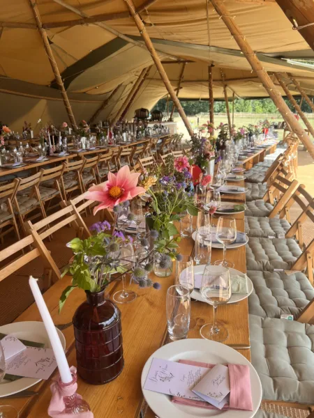 Colourful tipi wedding reception with festoon lights, bright florals, and wooden tables