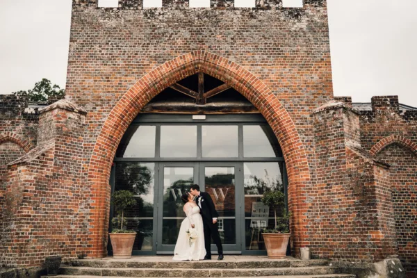 Bride and groom standing in a tall Gothic brick arch doorway at a wedding venue