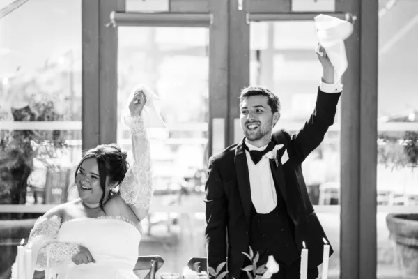 Black and white photo of a bride and groom celebrating with arms raised at their wedding reception