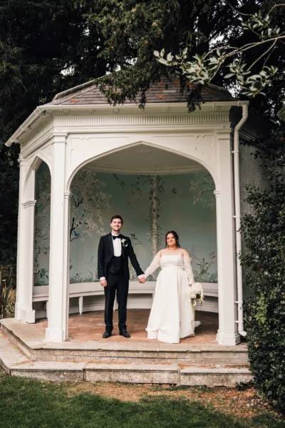 Bride and groom standing together under a white garden gazebo at a wedding venue