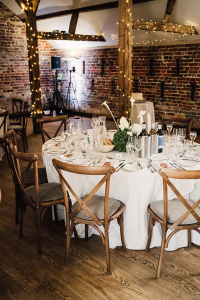 Rustic wedding barn interior with wooden cross-back chairs and dressed reception tables