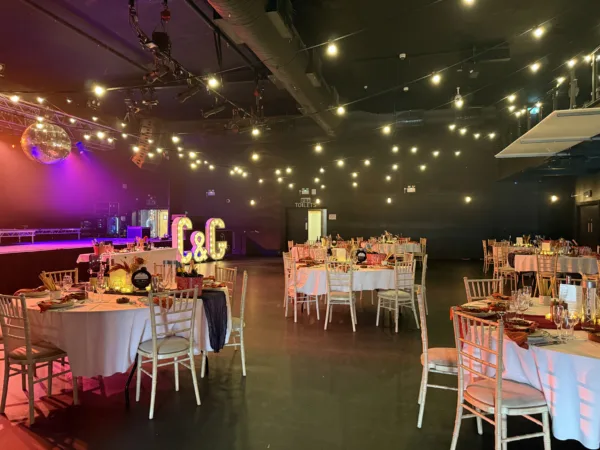 Wedding reception venue with warm string lights, purple ambience, and dressed tables