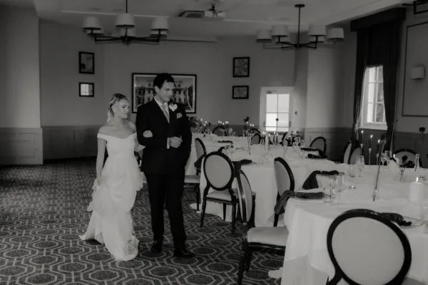 Black and white photo of a bride and groom standing in an elegant wedding reception room
