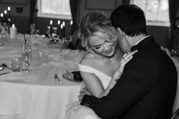 Black and white image of a bride seated at a candlelit wedding reception table with a decorative lamp