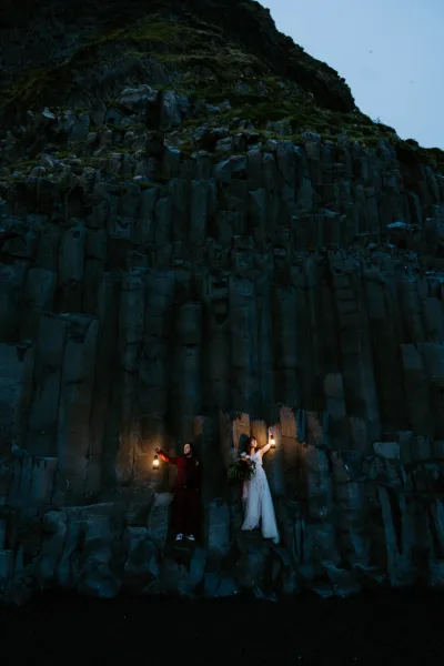 Bride and groom holding lanterns on rock stacks in Iceland on the beach