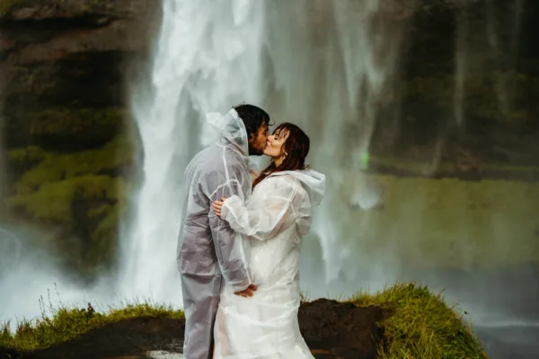 Bride and groom wearing waterproof ponchos so they don't get wet in from of seljalandsfoss