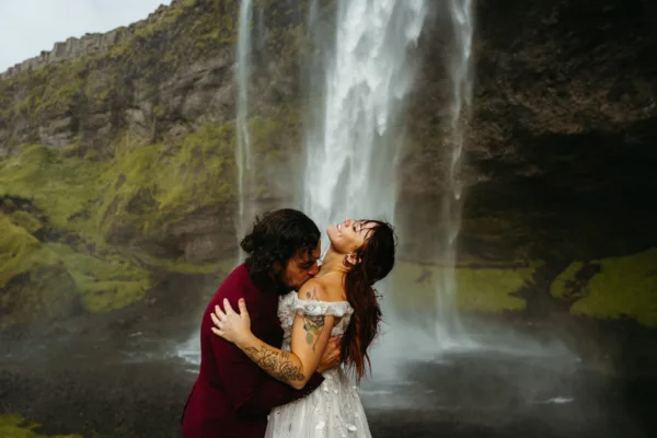Groom kissing bride's neck with greenery and Seljalandsfoss in the background