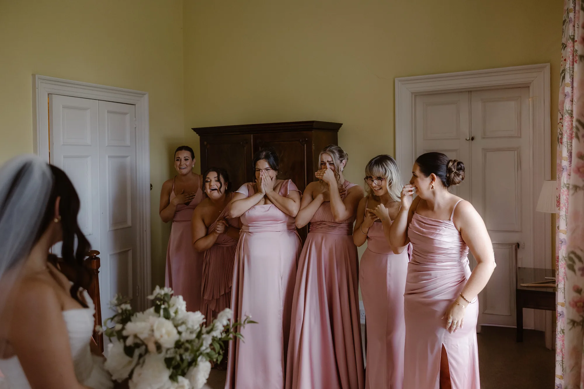 Sophie Dimitri Wedding Day Jono Symonds Photo Film 98 - Sophie & Dimitri's Beautiful, Relaxed & Elegant Wedding Weekend at Capesthorne Hall in Cheshire Bridesmaids in pink Amaze dresses looking delighted as they see the bride for the first time in her dress.