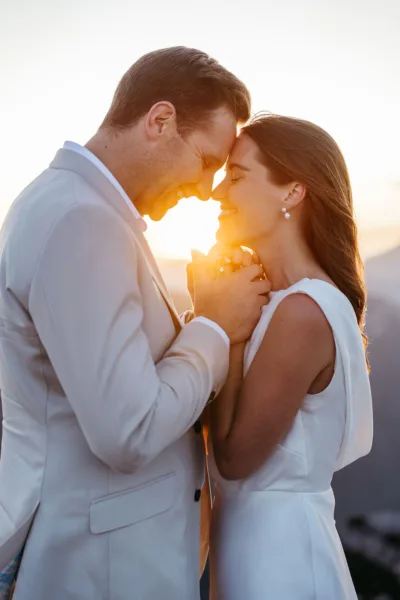 Bride and groom touching foreheads with the sun setting through them