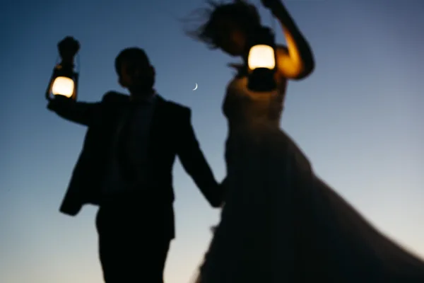 Silhouette of bride and groom holding lanterns on Cadini di Misurina during blue hour