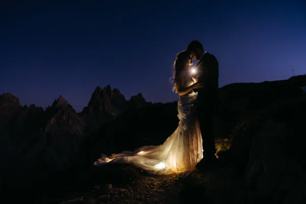 Backlit portrait of bride and groom, with fairy lights in bride's dress, at blue hour on Cadini di Misurina