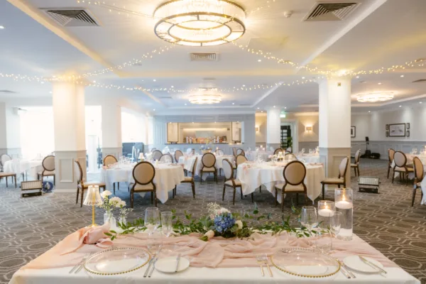 Candlelit wedding reception room with round tables dressed in white, pink florals, and fairy lights