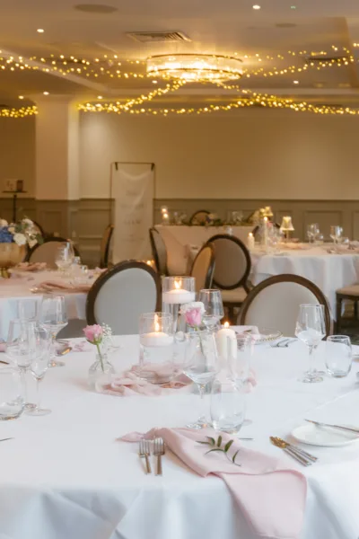 Elegant wedding reception tables with candles, pink flowers, and glassware under fairy lights