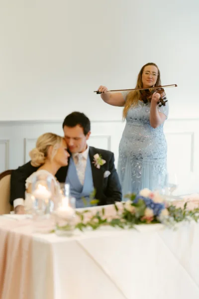 Violinist in a blue dress performing beside a bride and groom at the top table