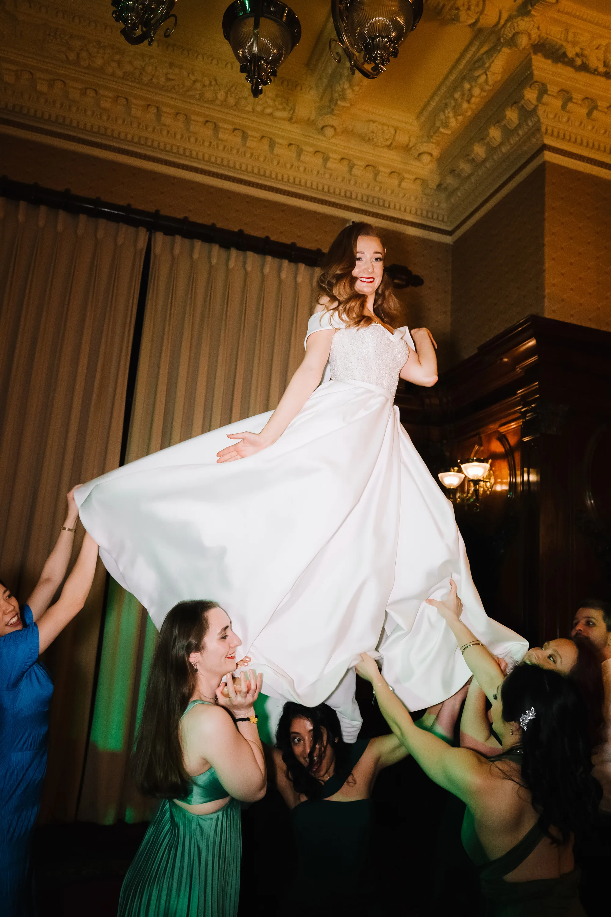 Bride being lifted into the air by guests on the dance floor during the evening wedding reception at Ashridge House.