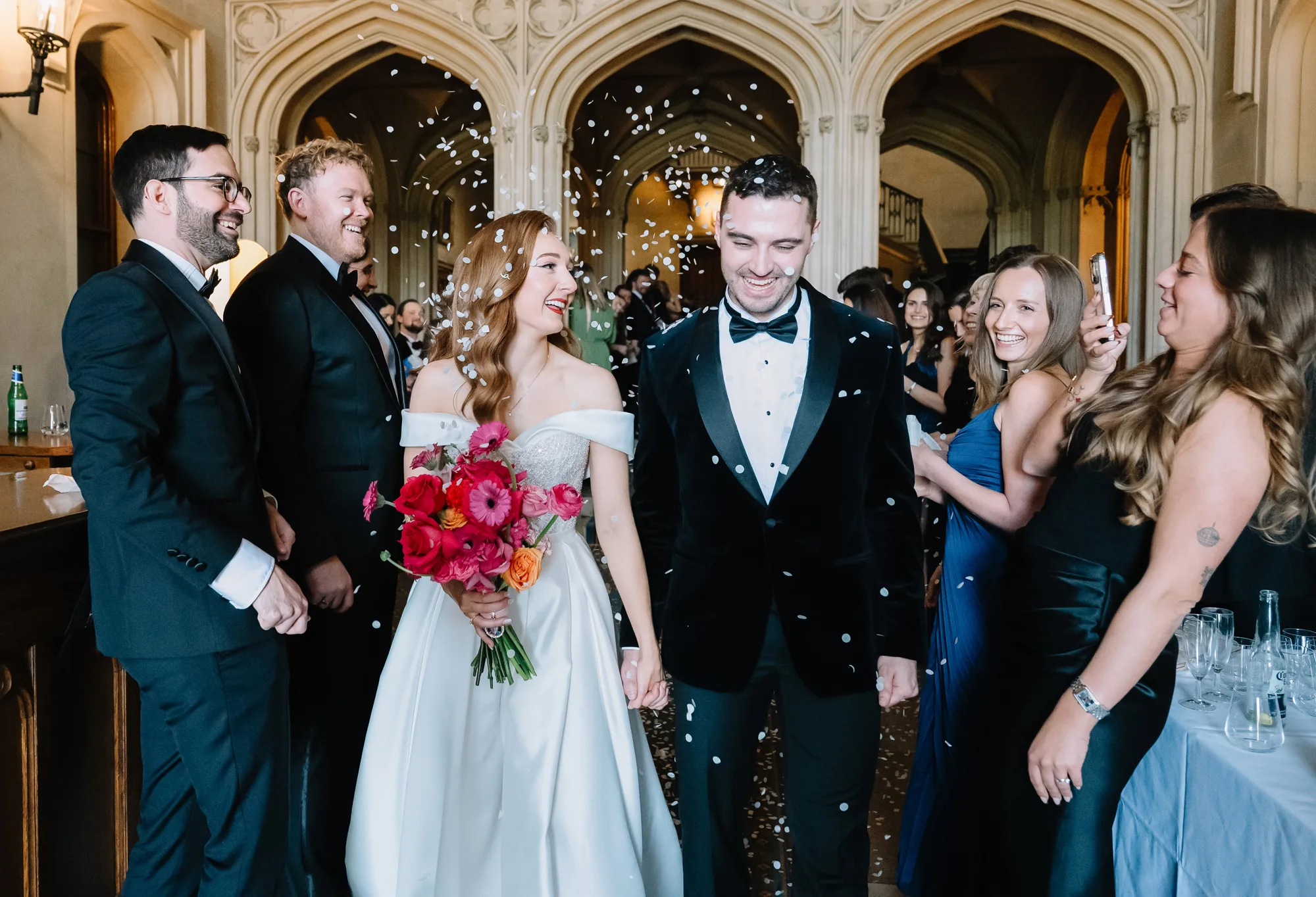 Bride and groom walk through a confetti shower at Ashridge House following their wedding ceremony.
