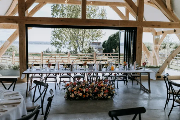 A wedding breakfast top table in a Kent wedding barn, with open bifold doors to the garden and coast