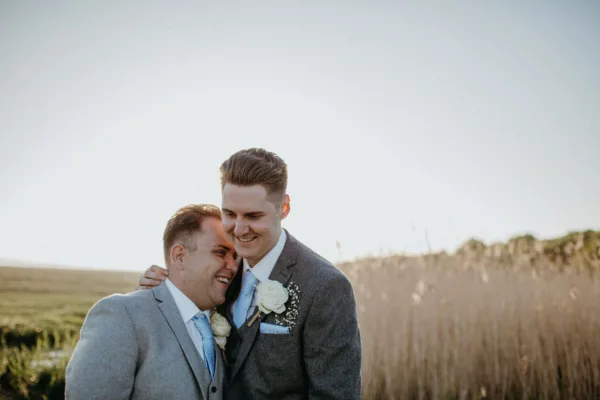 Grooms in front of tall grasses at The Harty Estate wedding venue