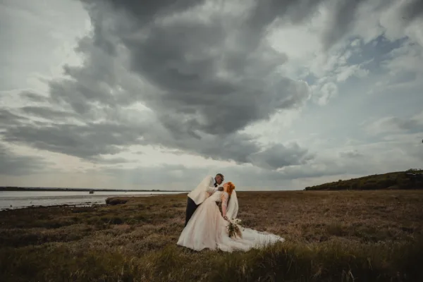 Bride and groom pose beneath a dramatic sky at a wedding venue on the Kent coast