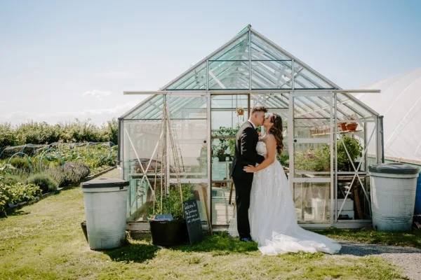 Bride and groom kiss in front of The Harty Estate greenhouse in the Kitchen Garden
