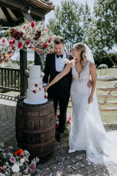 Newlyweds cut their wedding cake outdoors beneath a flower arch at The Harty Estate