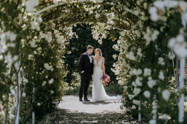 Bride and groom beneath a flowering rose tunnel at The Harty Estate Kent wedding venue