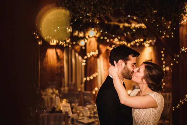 Newlyweds kiss in a fairy-lit wedding barn in Kent