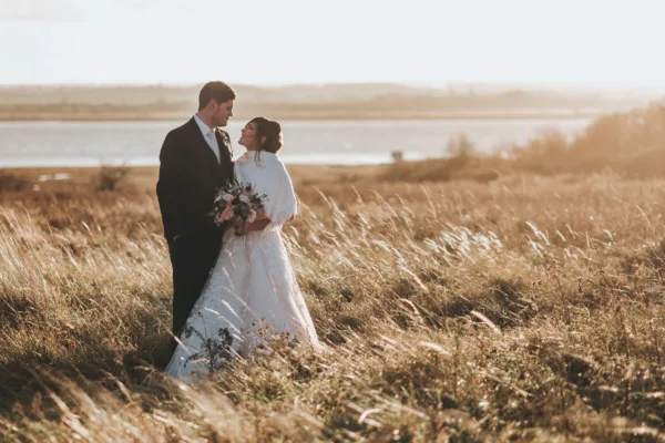 Newlyweds on their winter wedding day, standing in meadows in front of the Kent estuary