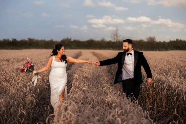 Newlyweds hold hands over the farmlands of The Harty Estate wedding venue