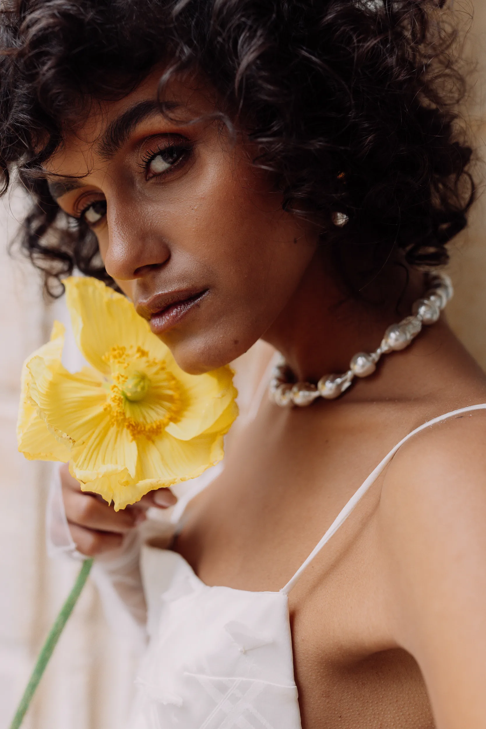 Beautiful Black model bride with a chunky pearl necklace and naturally loose wavy afro hair posing with a yellow Icelandic Poppy.