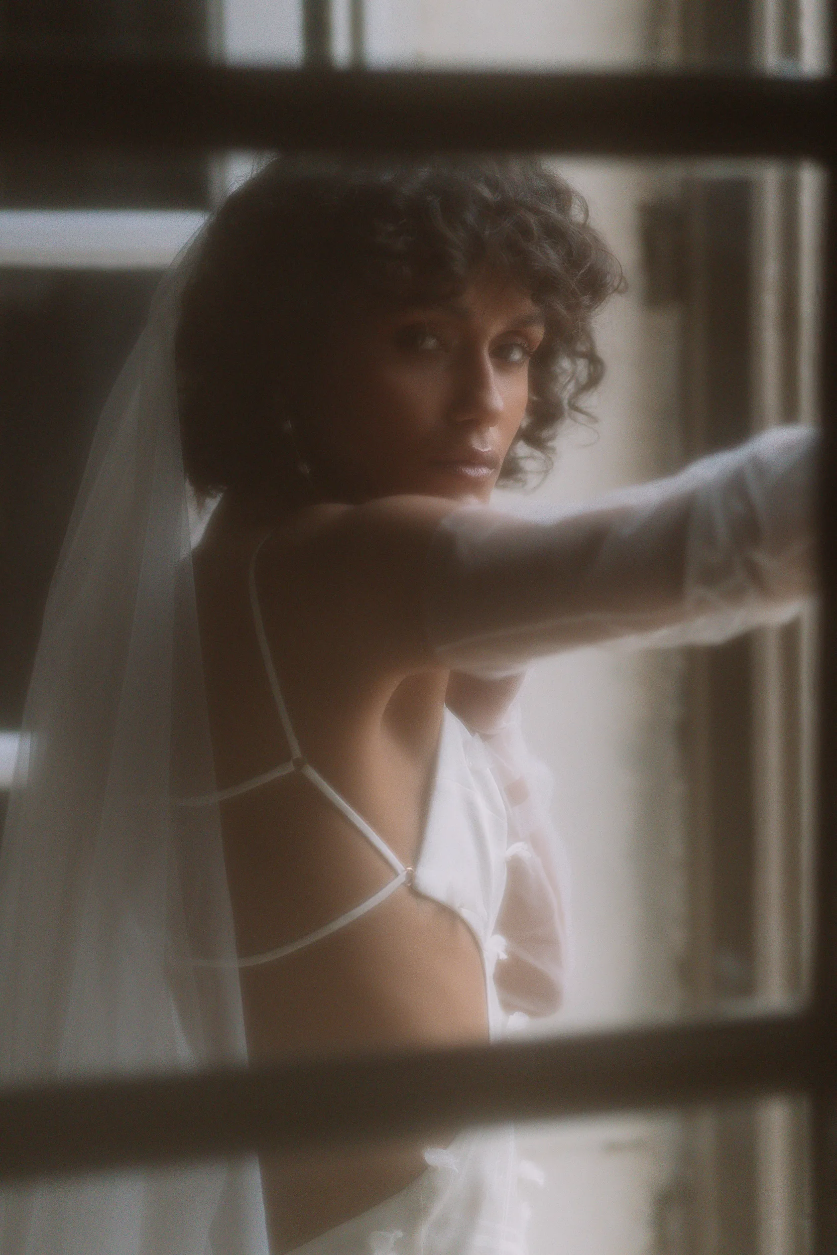 Beautiful Black model bride wearing a backless dress and long tulle gloves. Her naturally curly afro hair is loose and wavy.