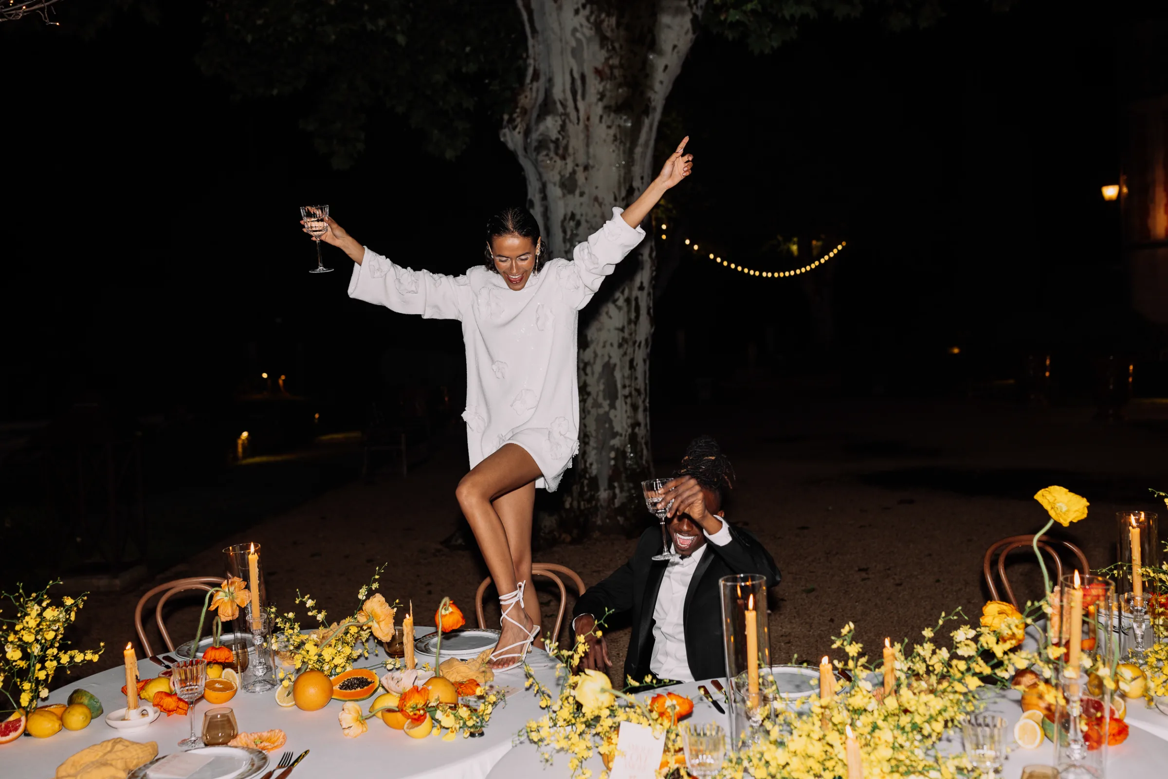 Black Bride dancing on a beautifully styled wedding reception table while the groom raises a glass at Le Mas d'Arvieux.