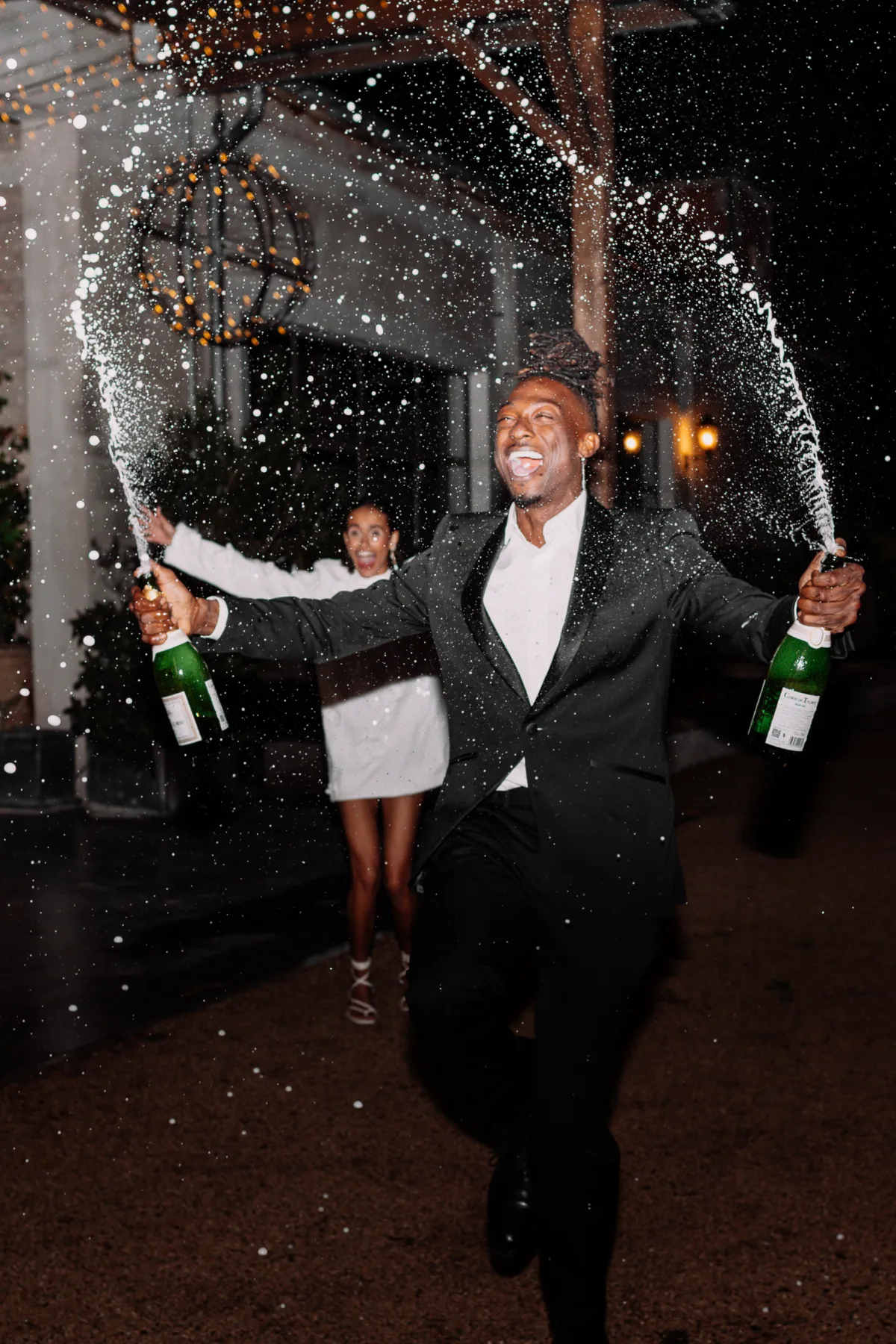 Groom spraying champagne as the bride celebrates behind him during the evening wedding reception at Le Mas d'Arvieux.
