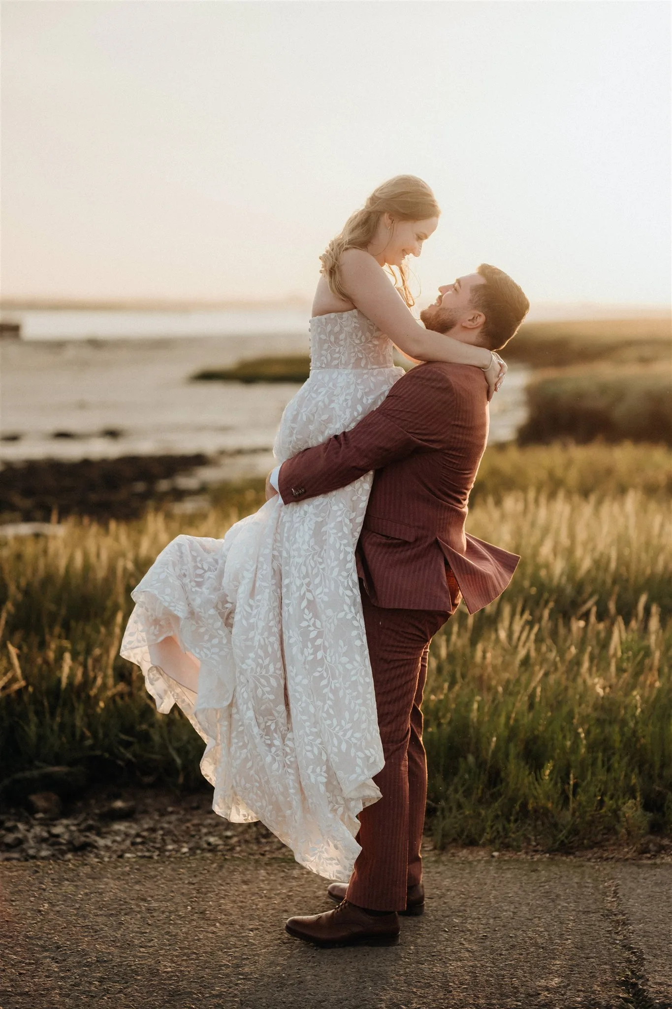 Groom lifts his bride in front of the estuary during their wedding in Kent