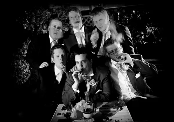 Six groomsmen smoking cigars together in a black-and-white wedding photograph.
