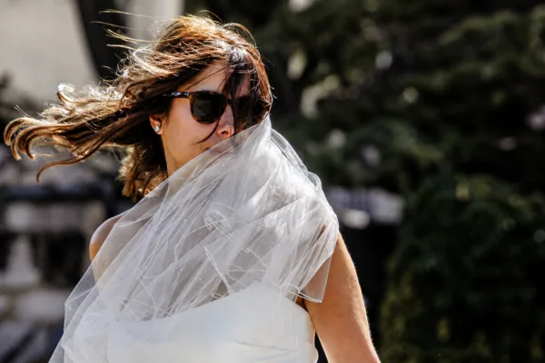 Bride wearing sunglasses with her veil blowing across her face